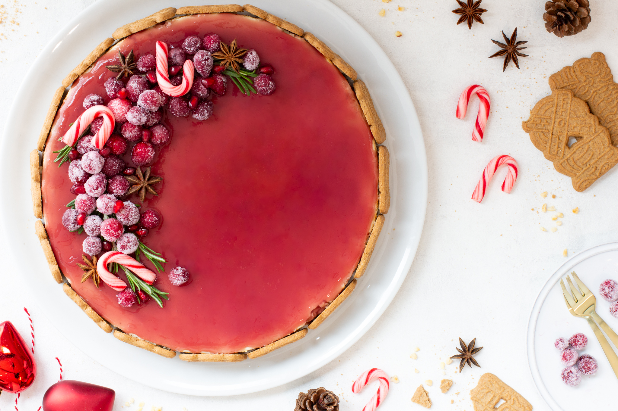 Spekulatius Cheesecake mit einem Granatapfelspiegel und einem opulenten Fruchttopping aus kandierten Cranberries, Granatapfelkernen, Sternanis und Rosmarin, von oben fotografiert