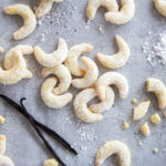 Ein Haufen Vanillekipferl und zwei Vanillestangen verteilt auf der Arbeitsplatte