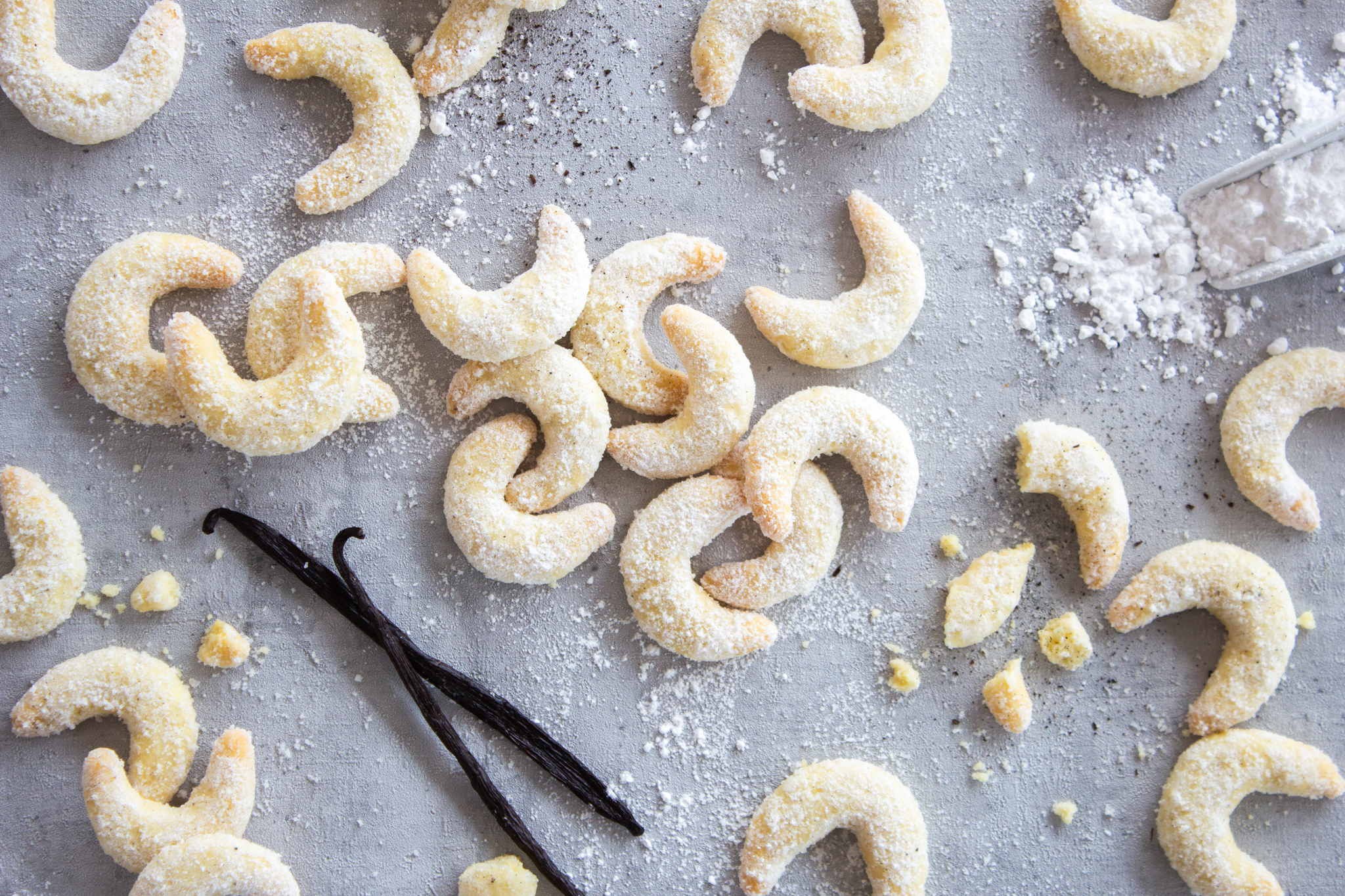 Ein Haufen Vanillekipferl und zwei Vanillestangen verteilt auf der Arbeitsplatte
